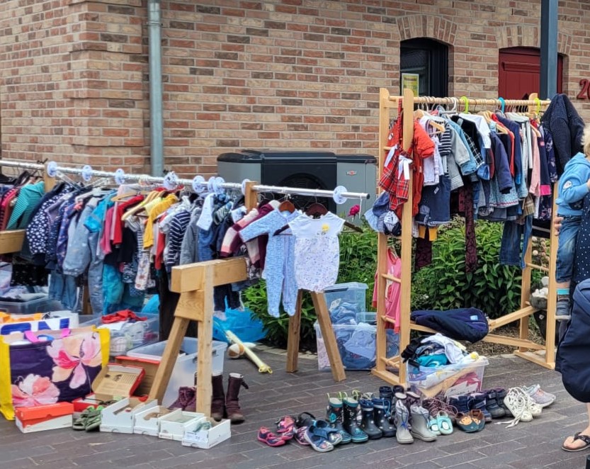 Flohmarktstand mit Kleidung auf einer Kleiderstange auf einer Auffahrt vor einem Haus